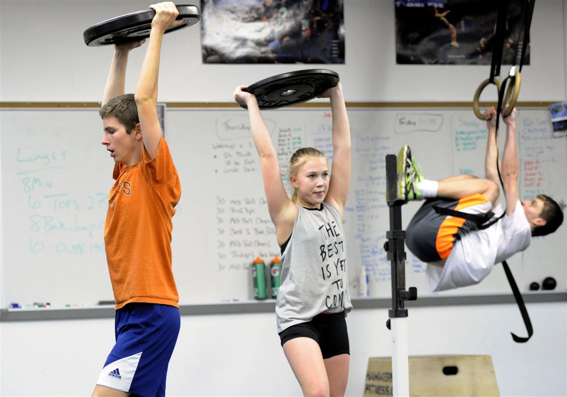 Dan Jackson, 16, left, Amelia Enfinger, 14, center, lift weights over their heads while doing squats in a CrossFit class for teens in Loyalhanna.