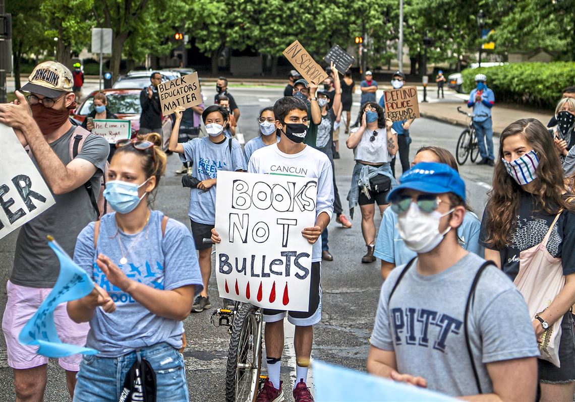 In this file photo, protesters hold signs and wear masks as they listen to a speaker during the 
