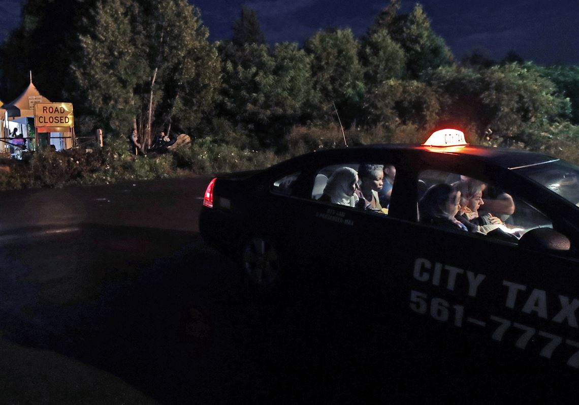 In this Aug. 8 file photo, a taxi filled with women from various nations paying their fare as they arrive at an unofficial border station across from Saint-Bernard-de-Lacolle, Quebec, on Roxham Road in Champlain, N.Y.