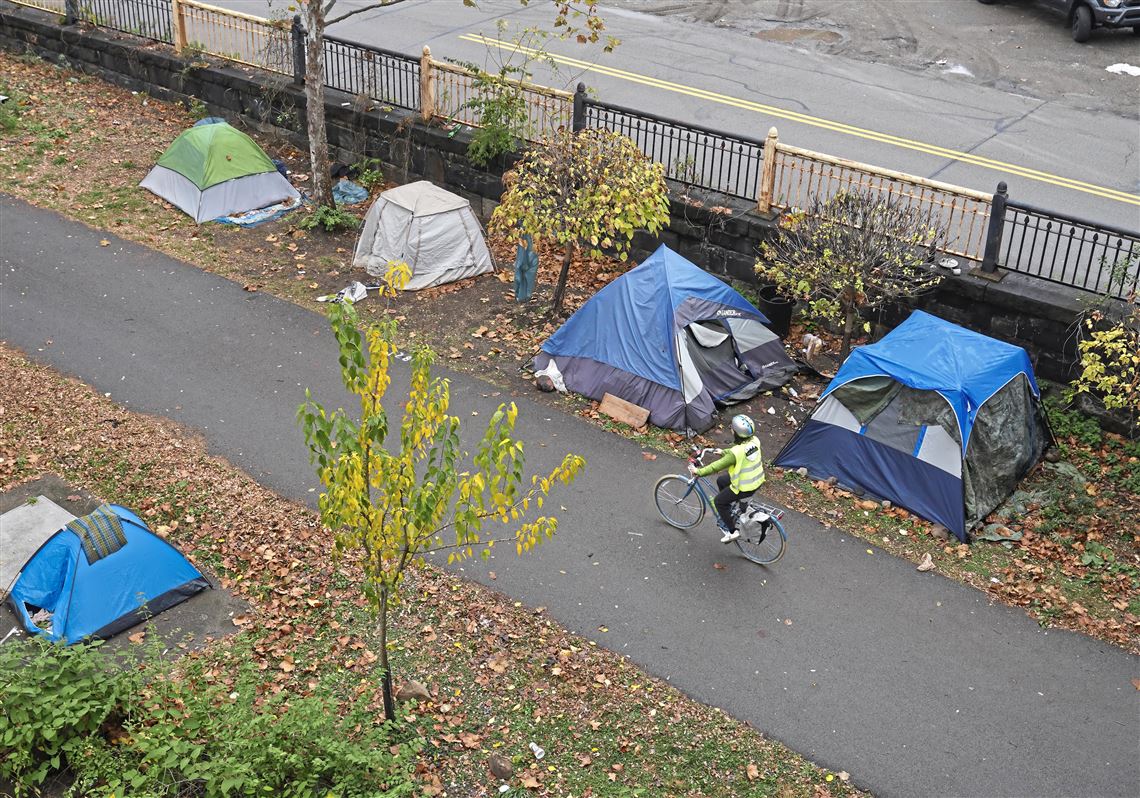 A cyclist passes by a homeless encampment along the Three Rivers Heritage Trail on the North Shore by the 16th St. bridge Friday, Nov. 15, 2024. 