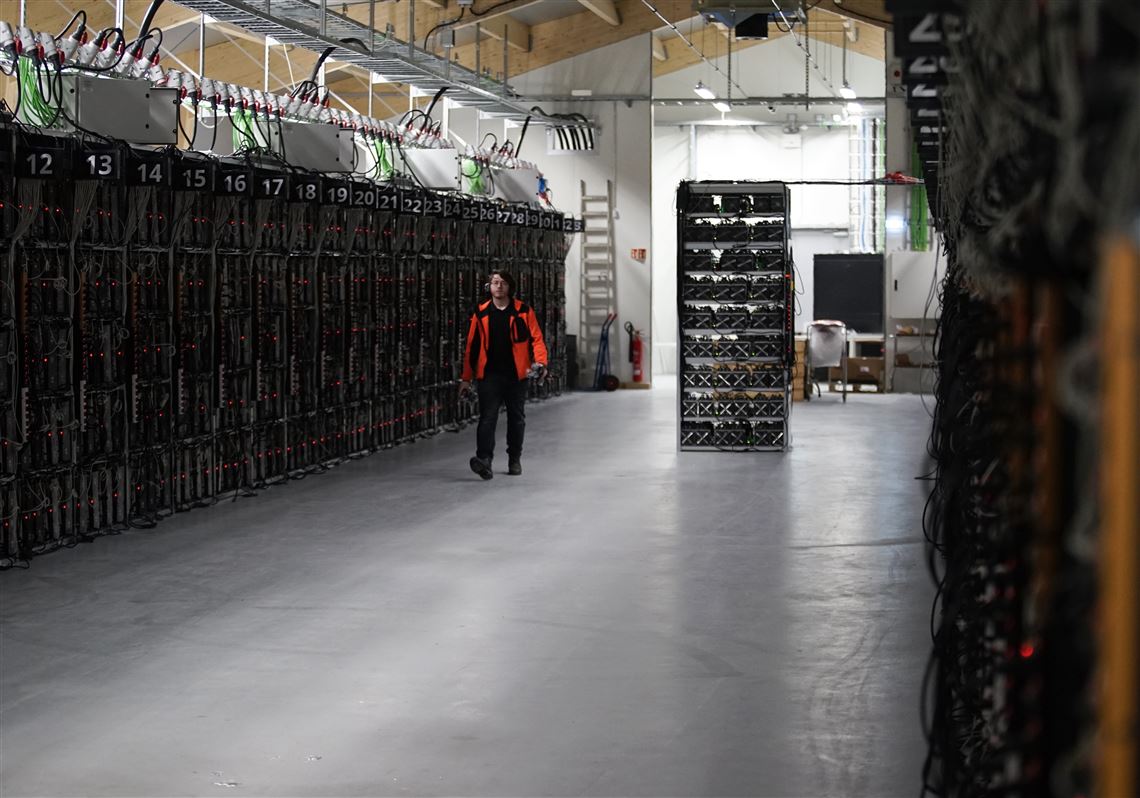 In this photo taken on Jan. 17, 2018, a worker walks along a row of computer rigs that run around the clock 'mining' bitcoin inside the Genesis Mining cryptocurrency mine in Keflavik, Iceland. Hand in hand with the rise of bitcoin is a soaring cost of â€œmining