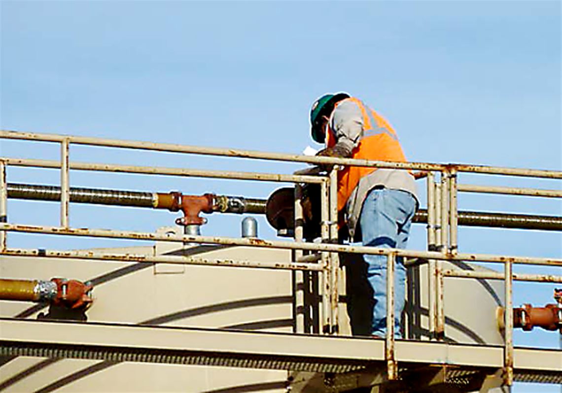 A worker examines a tank through an open hatch.