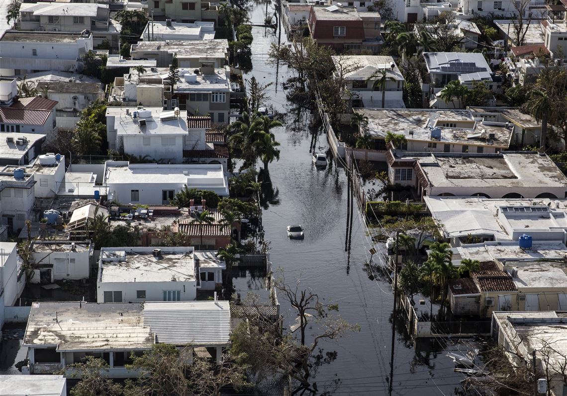 In this Sept. 25 file photo, a vehicle in  San Juan, Puerto Rico, drives through streets filled with floodwater near destroyed homes from Hurricane Maria.