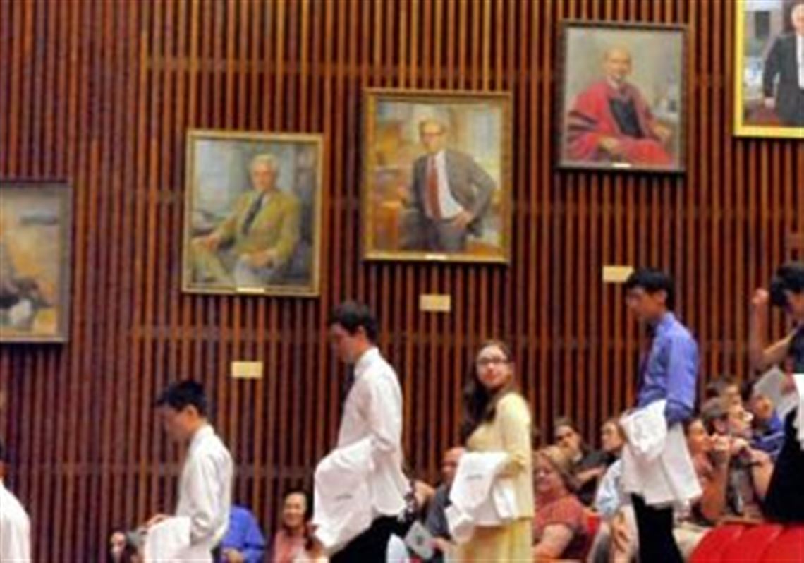 Incoming University of Pittsburgh School of Medicine students at the 15th annual White Coat Ceremony in 2013 stand under the watchful portraits of the school's past deans.