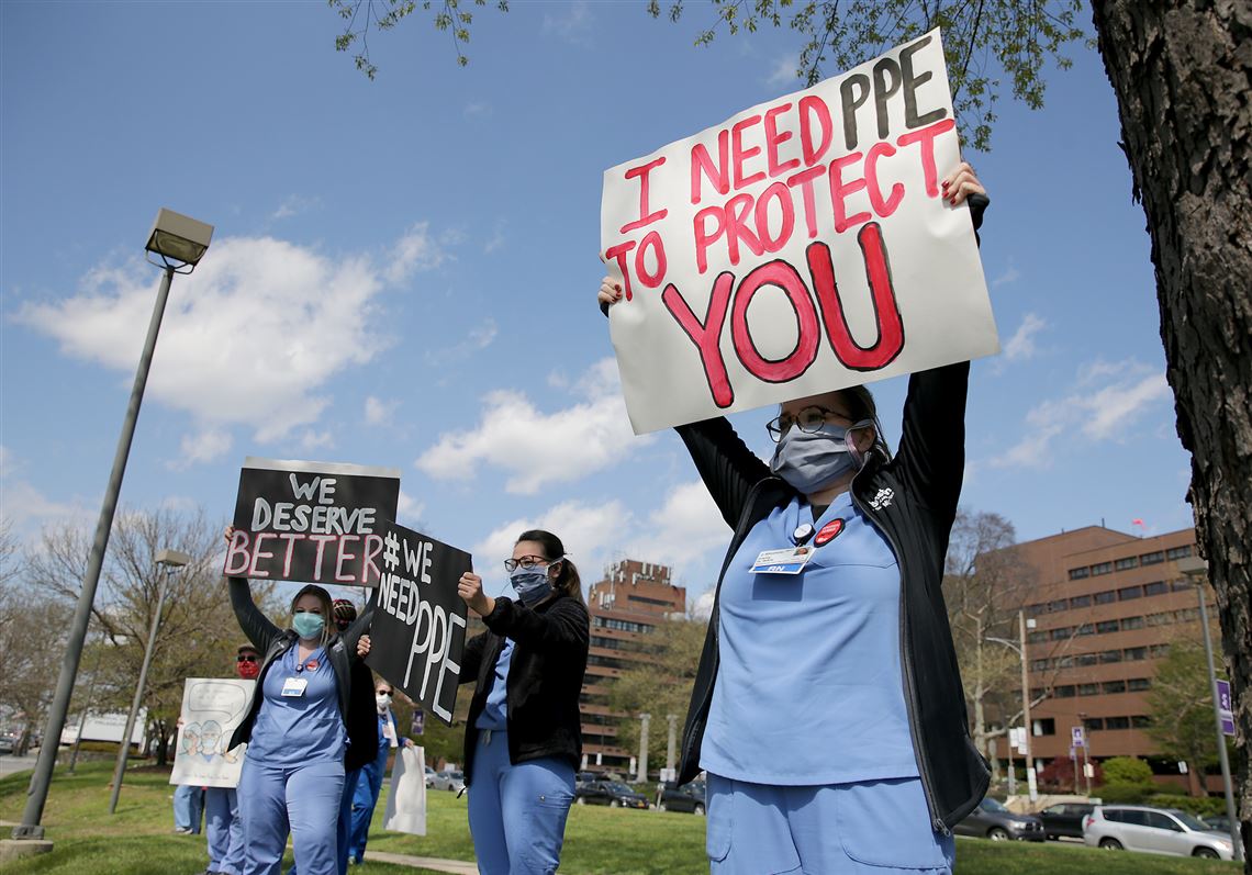 In this April 15, 2020, photo, Carly Heller, an ICU nurse at Einstein, at right, holds up a sign with her coworkers outside Einstein Medical Center in Philadelphia.