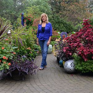 Marie Tuma stands on the sidewalk leading to the front door of her house, surrounded by a few of the many plants she grows in her large garden in Monaca. 