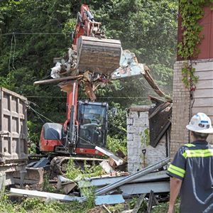 Jadell Minniefield of Hazelwood, owner of Jadell Minnifield Construction Services Inc., left, operates an excavator as he works to demolish an abandoned home, which has recently tested positive for lead contamination, while employee Roger Marva of Hazelwood, right, watches from the road, Tuesday, July 2, 2019, in Braddock Hills.