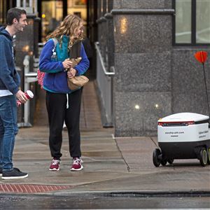 University of Pittsburgh students Ryan Kasper, left, and Adele Stefanowicz, both of Oakland, laugh as they watch a Starship Technologies on-demand delivery service autonomous robot struggle to get from the road to the sidewalk on Nov. 7, 2019 in Oakland