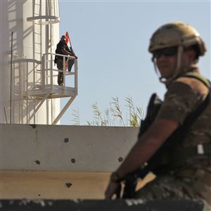 A member of the Iraqi government forces' stands guard at a humvee turret as another raises the Iraqi national flag from an oil silo at the Bai Hassan oil field, west of the multiethnic northern Iraqi city of Kirkuk, on October 19, 2017.