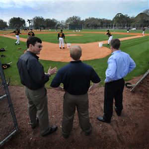 Pirates owner Bob Nutting, left, general manager Neal Huntington and president Frank Coonelly, right, huddle behind home plate to watch the workouts in 2010 at Pirate City in Bradenton, Fla.