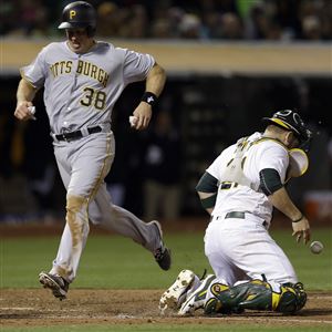 The Pirates' Erik Kratz, left, scores behind Athletics catcher Stephen Vogt during the 10th inning Saturday in Oakland, Calif.