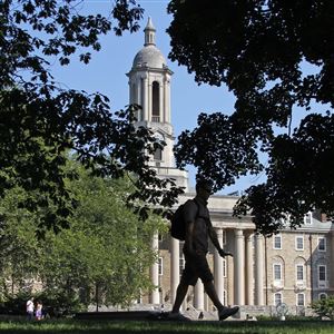 A Penn State University student walks across campus in front of Old Main on main campus in State College.