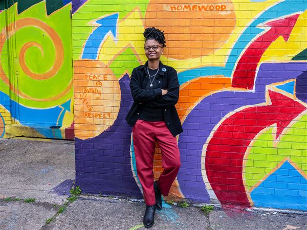 Angelica Anderson leans against a colorful mural behind the Afro American Music Institute in Homewood.